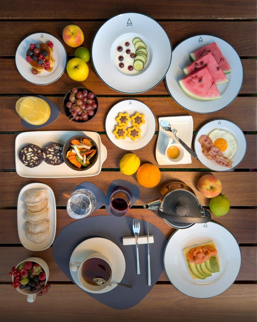 Colazione in suite: frutta, pancake, toast e caffè su tavolo in legno.